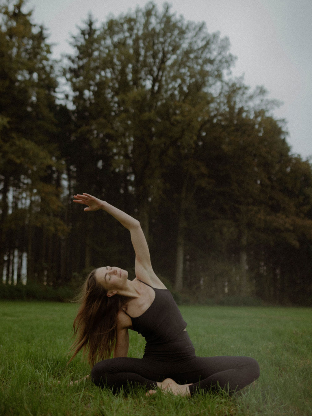 Person streckt die Arme in einer Yoga-Pose im Wald bei Sonnenlicht